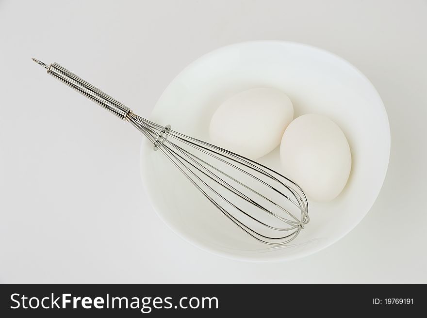 An image of two white eggs and a whisk