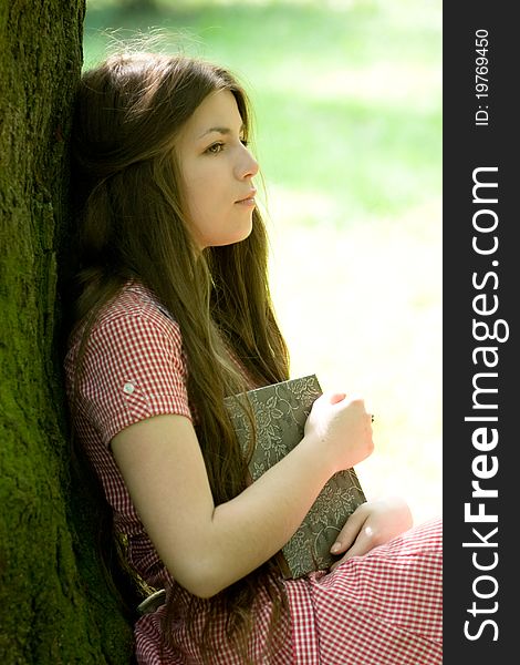 Attractive girl is sitting with book in the park and thinking or dreaming. Attractive girl is sitting with book in the park and thinking or dreaming
