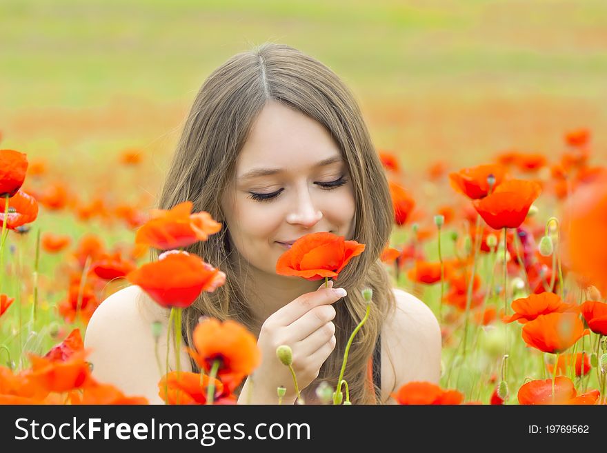 A young woman on field of poppies in summer, sniffing or are regarding a flower. She has a healthy facial skin. A young woman on field of poppies in summer, sniffing or are regarding a flower. She has a healthy facial skin