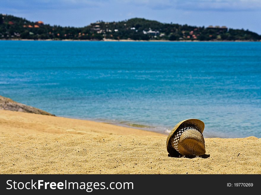 Straw hat on white sand of coast against the sea and the blue sky