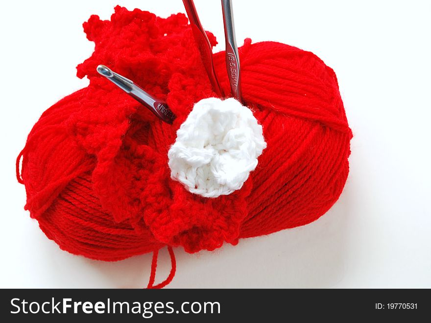 Ball of red yarn with crocheting hooks and white crocheted flower  . Ball of red yarn with crocheting hooks and white crocheted flower