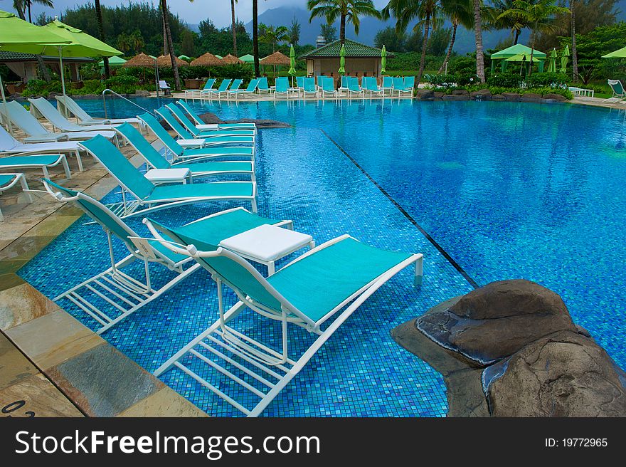 Turquoise chairs sitting in a deep blue swimming pool surrounded by green umbrellas at an upscale resort in Kauai, Hawaii. Turquoise chairs sitting in a deep blue swimming pool surrounded by green umbrellas at an upscale resort in Kauai, Hawaii
