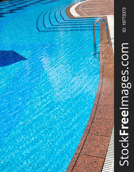 A portrait of blue tile swimming pool with steps and staircase entrance with marble edging. A portrait of blue tile swimming pool with steps and staircase entrance with marble edging