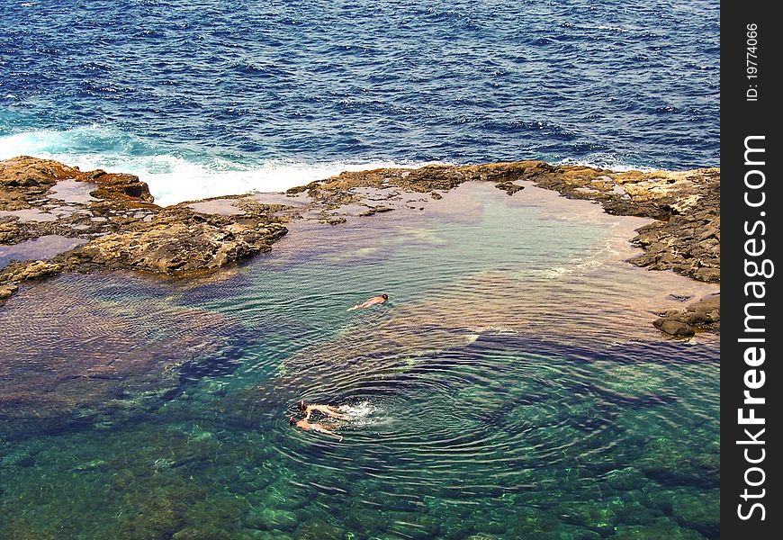 People diving in a natural basin in the rocks coastline of Lanzarote