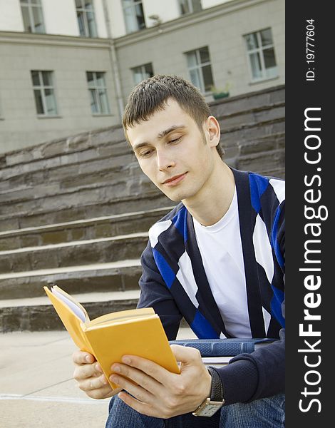 Closeup of an attractive male student on campus sits on the stairs with books. Closeup of an attractive male student on campus sits on the stairs with books