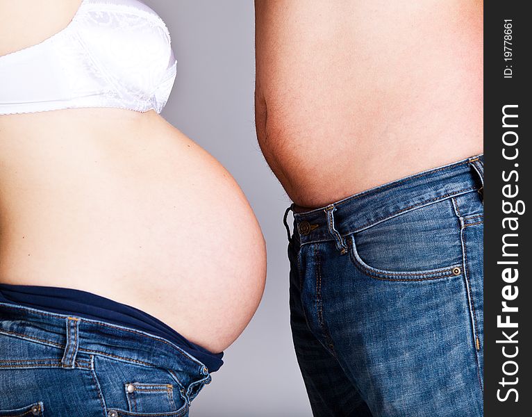 Man and pregnant woman bellies on gray