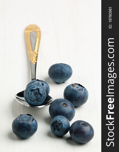 Teaspoon with fresh blueberries on white wooden table