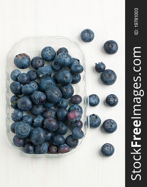 Top view on plastic box with fresh blueberry on white wooden table