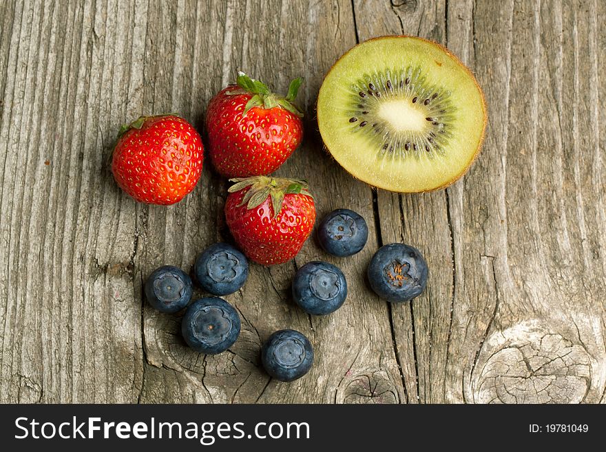 Top view on fresh strawberries, blueberries and kiwi on old wooden table