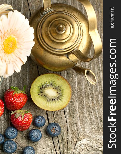 Top view on fresh strawberries, blueberries and kiwi with old vintage teapot on old wooden table. Top view on fresh strawberries, blueberries and kiwi with old vintage teapot on old wooden table