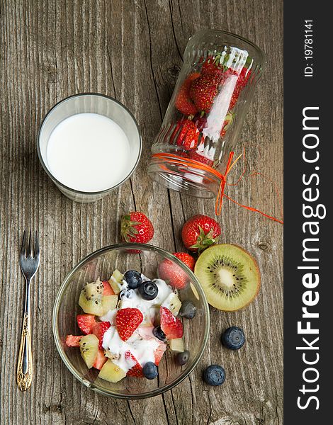 Top view on bowl of fruit salad with fresh strawberries, blueberries and kiwi with glass of milk on old wooden table table. Top view on bowl of fruit salad with fresh strawberries, blueberries and kiwi with glass of milk on old wooden table table