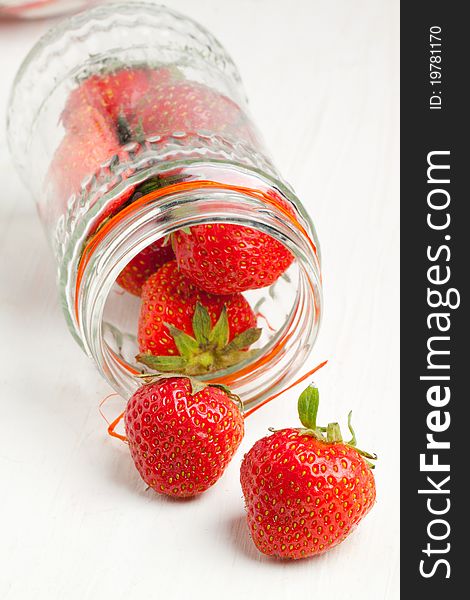 Glass pot of fresh strawberry on white wooden table