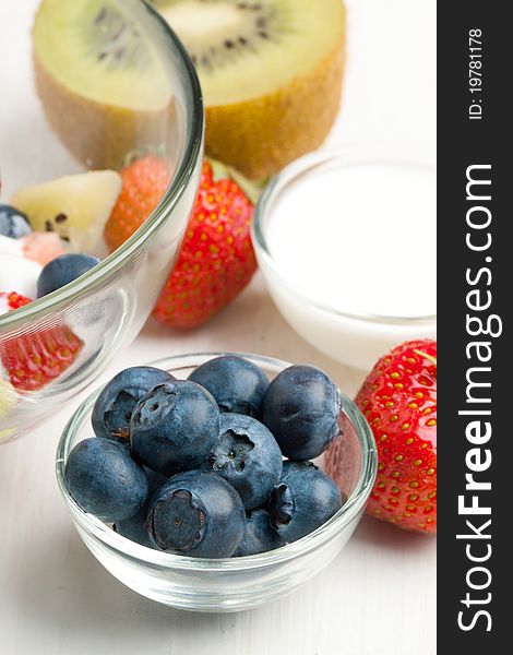 Glass bowl of fresh strawberries, blueberries and kiwi with whipped cream on white table. Glass bowl of fresh strawberries, blueberries and kiwi with whipped cream on white table