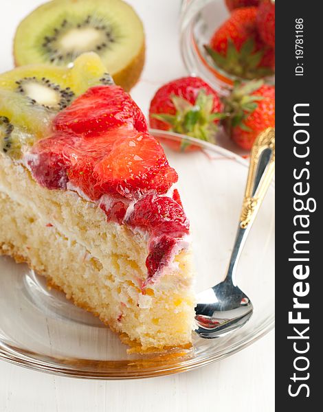 Piece of homemade fruit cake with strawberries and kiwi on white wooden table