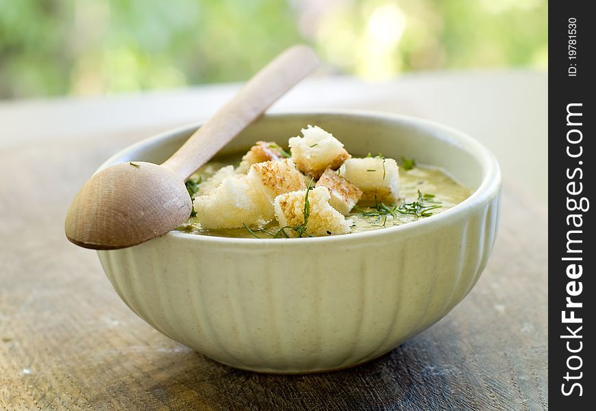 A bowl of green vegetable soup with croutons and dill
