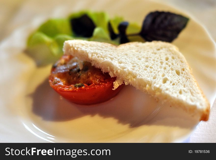 Appetizer - a baked tomato with piece of toast and salad on a white porcelain plate. Appetizer - a baked tomato with piece of toast and salad on a white porcelain plate