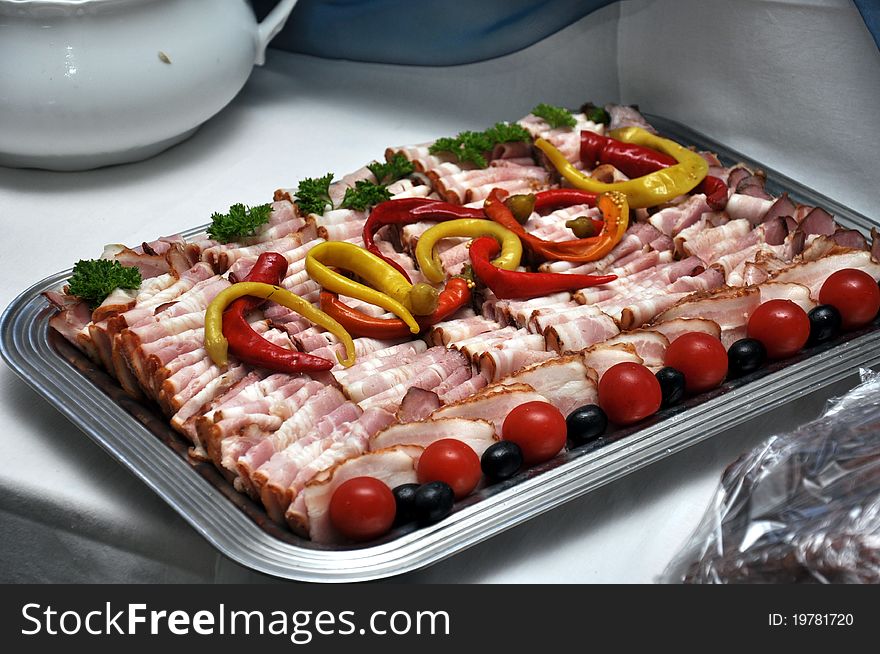 A tray full of bacon and flitch, decorated with cherry tomatoes, black olives and chilli peppers. A tray full of bacon and flitch, decorated with cherry tomatoes, black olives and chilli peppers