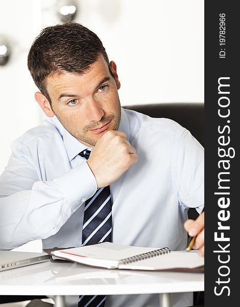 Pensive young businessman with pen in office. Pensive young businessman with pen in office