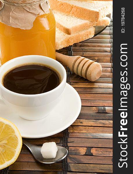 Coffee, honey, lemon and bread on straw table
