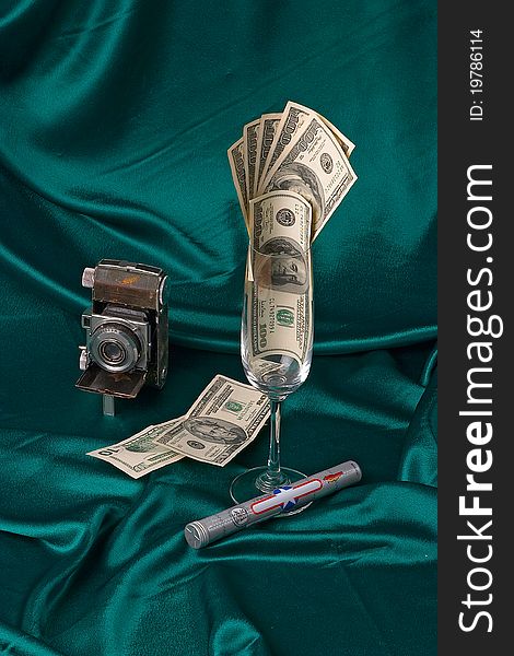 Composition shot of money, camera and cigar on green silk background