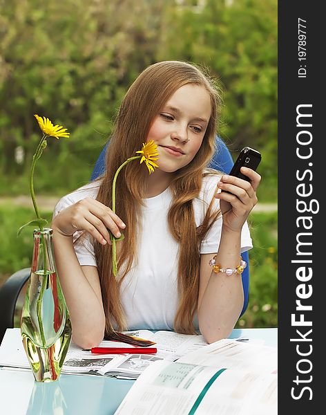 The young girl with a fair hair prepares for examinations and reads the message in a mobile phone. The young girl with a fair hair prepares for examinations and reads the message in a mobile phone