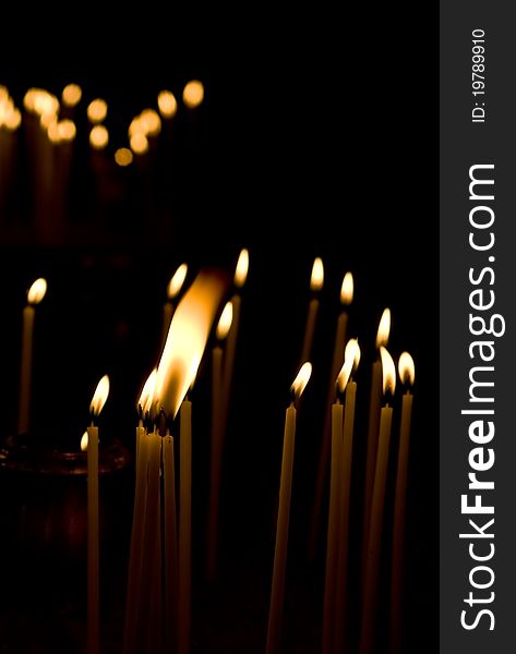 Burning votive candles in a Greek church over dark background. Burning votive candles in a Greek church over dark background.