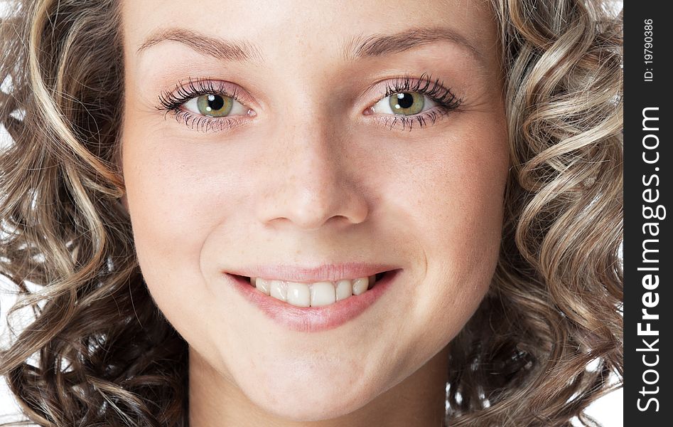 Closeup portrait of a smiling young woman (18s). Green eyes, toothy smile and curly hair