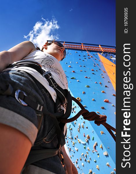 Young girl in climbing equipment standing in front of a artificial climbing wall. Young girl in climbing equipment standing in front of a artificial climbing wall