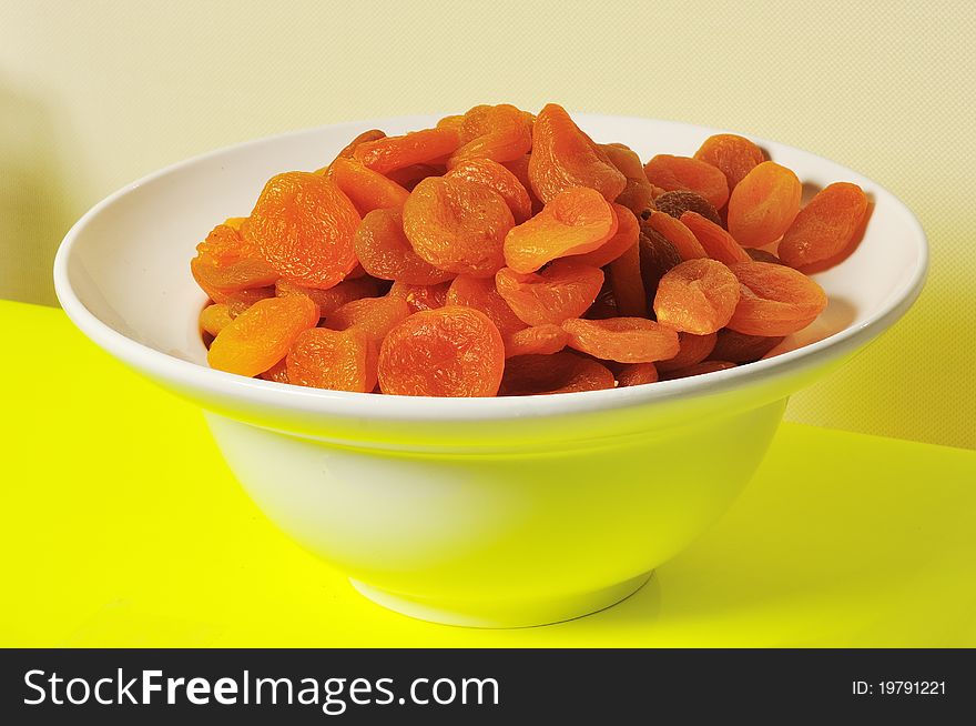 Dried apricots are in a deep white plate against a yellow background