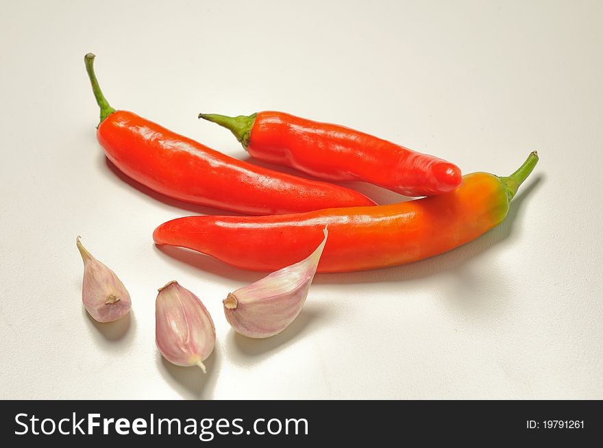 Three red hot pepper and three cloves of garlic against a white background. Three red hot pepper and three cloves of garlic against a white background