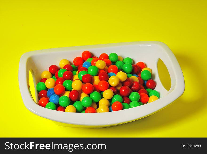 Children's chewing gum in the form of colored balls lie in a deep white plate. Children's chewing gum in the form of colored balls lie in a deep white plate