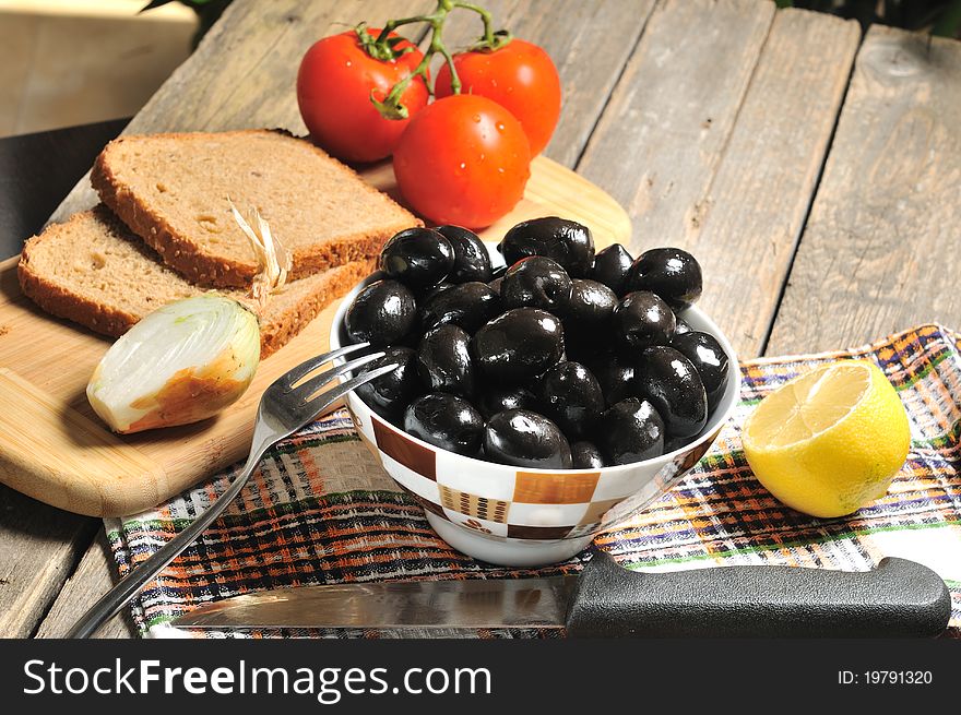 Black olives, bread, onions, tomatoes and lemon on a rustic table