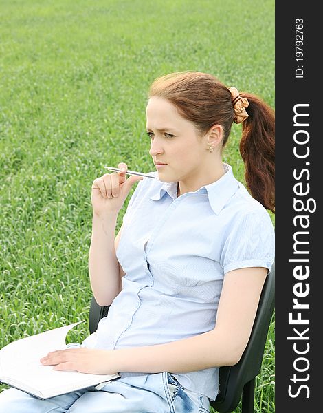 The girl sitting in the field and wrote in a notebook