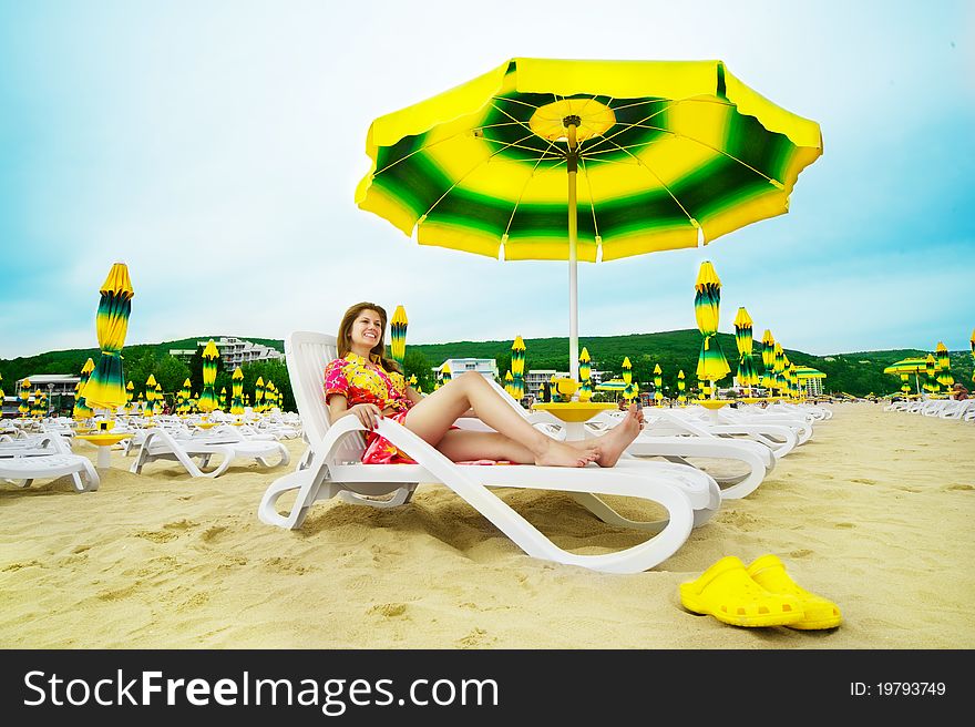 Beautiful happy woman in colourful clothes is laying on the sunbed on the beach under umbrella. Wide angle shot. Beautiful happy woman in colourful clothes is laying on the sunbed on the beach under umbrella. Wide angle shot.