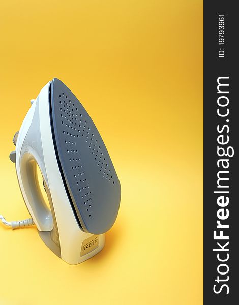 Closeup of gray modern electric iron on yellow background