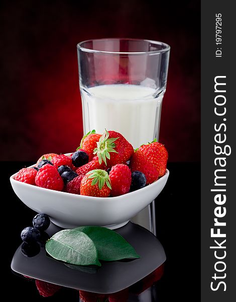 Photo of milk glass with berries on red lighted background. Photo of milk glass with berries on red lighted background