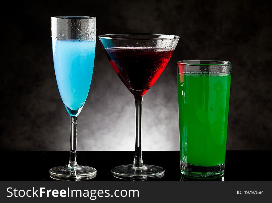 Photo of three cocktails on black glass counter with grey lighted background