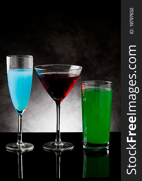 Photo of three cocktails on black glass counter with grey lighted background