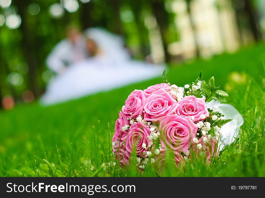 Bridal bouquet on a green meadow against the blurred newlyweds. Bridal bouquet on a green meadow against the blurred newlyweds