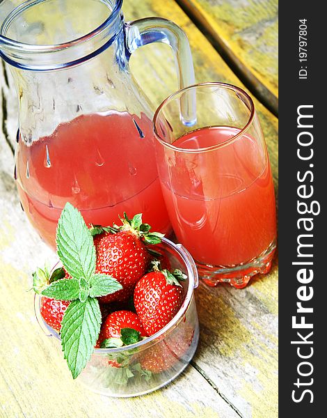 Strawberry juice in a glass pitcher and glass, next to a bowl of strawberries on a wooden table.Top view. Strawberry juice in a glass pitcher and glass, next to a bowl of strawberries on a wooden table.Top view