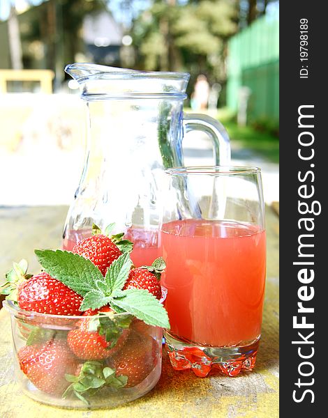 Strawberry juice in a glass pitcher and glass, next to a bowl of strawberries on a wooden table. Strawberry juice in a glass pitcher and glass, next to a bowl of strawberries on a wooden table