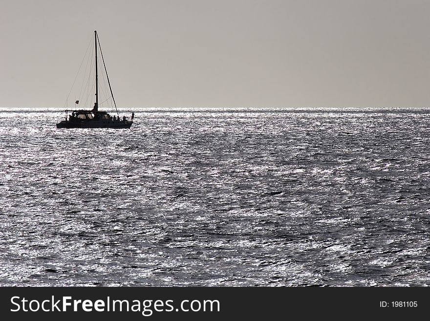 The last of the day's sunlight glints on the ocean and silhouttes a catamaran motoring into the dusk. The last of the day's sunlight glints on the ocean and silhouttes a catamaran motoring into the dusk.