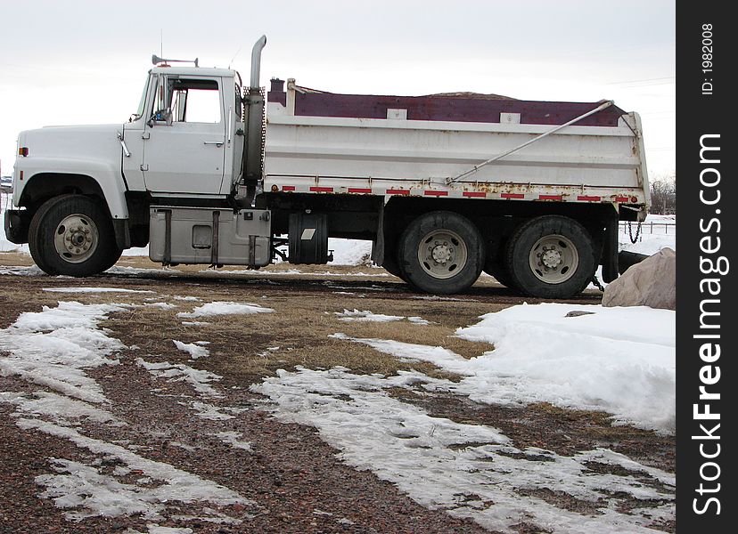 A side view of a white gravel truck parked outside after a delivery trip.