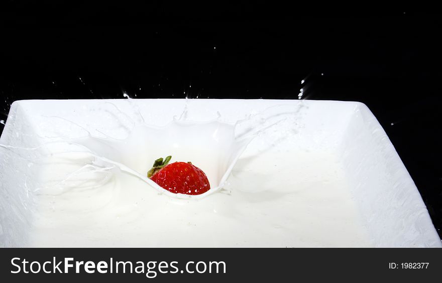 Fresh strawberry dropping into a dish of cream making a splash. Fresh strawberry dropping into a dish of cream making a splash
