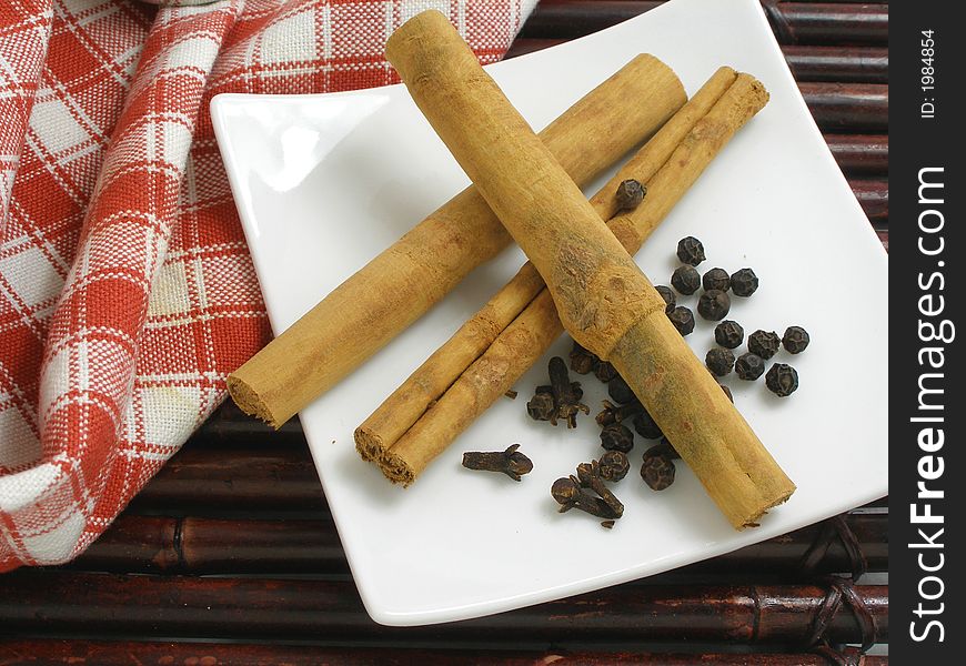 Cinnamon sticks with cloves and black peppercorns in a square plate. Cinnamon sticks with cloves and black peppercorns in a square plate