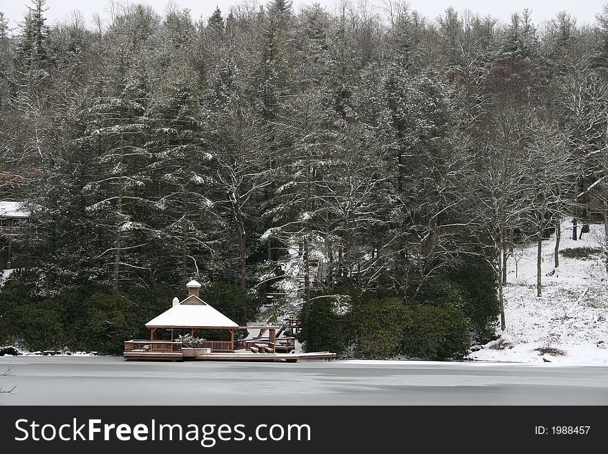 A snowy gazebo overlooking a partially frozen lake.