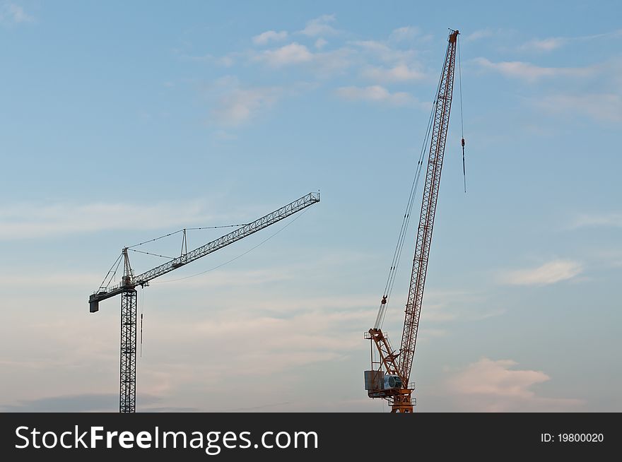 Two large cranes stand against a blue sky with clouds in the evening. Two large cranes stand against a blue sky with clouds in the evening.