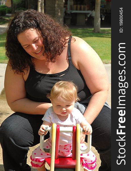 A mother and her toddler play on a tetter-totter in the park on a sunny day. A mother and her toddler play on a tetter-totter in the park on a sunny day.