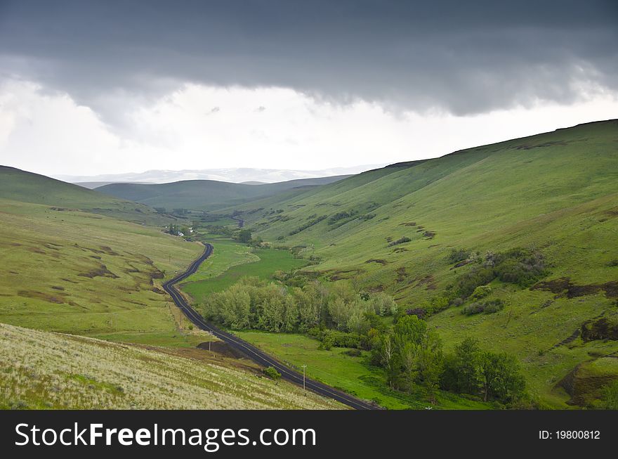 Black gravel road among grassy hills below a stormy sky. Black gravel road among grassy hills below a stormy sky