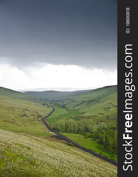 Black gravel road among grassy hills below a stormy sky. Black gravel road among grassy hills below a stormy sky